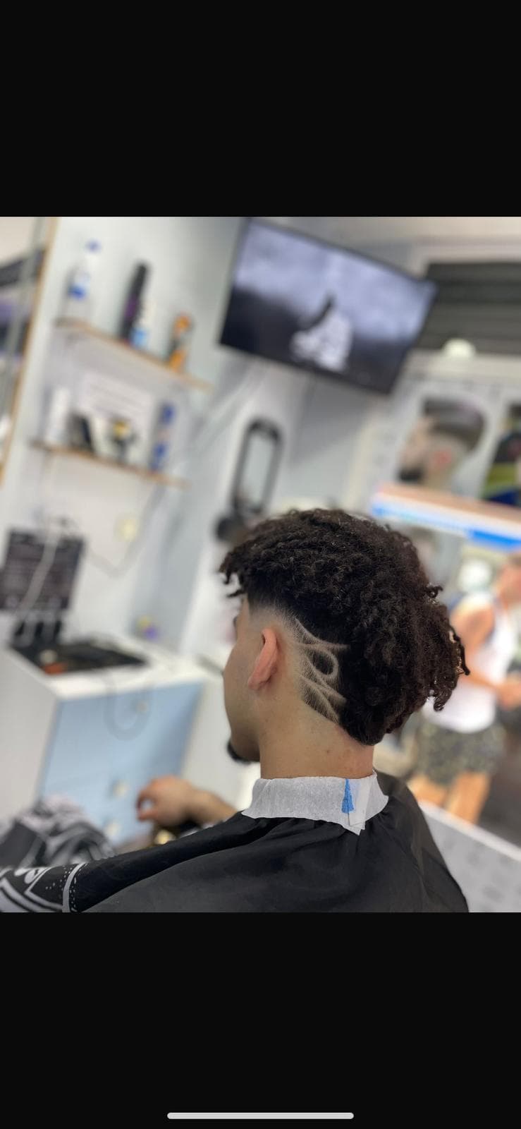 Joven con cabello rizado y diseño rapado artístico en un corte de pelo degradado.